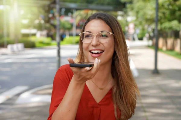 stock image Brazilian student girl recording voice message on smartphone, talking with colleagues, friends online in modern sustainable city street