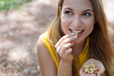 Beautiful healthy girl eating cashew nuts in the park. Looks to the side.