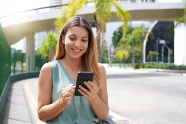 Pretty young woman using mobile phone walking in the streets of Sao Paulo, Brazil