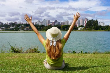 Barigui Park, Curitiba, Brezilya 'da çimlerin üzerinde oturan şapkalı genç bir kadın.