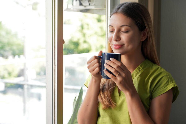 Relaxed beautiful young woman smelling her herbal tea at home in the morning