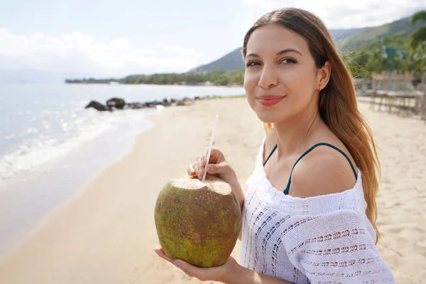 Close-up of relaxed woman drinking fresh coconut water on the beach enjoying a summer breeze