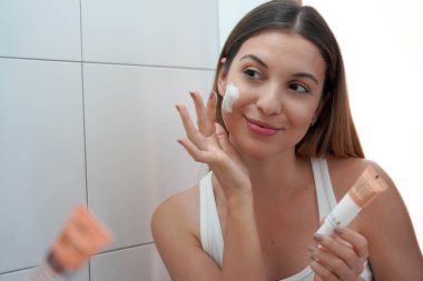 Sabah rutini. Güzel kız aynaya bakıyor ve yüz kremi kullanıyor..