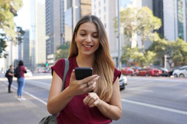 Brezilyalı kendine güvenen iş kadını Paulista Avenue, Sao Paulo, Brezilya 'da internet bankacılığı için cep telefonu kullanıyor.