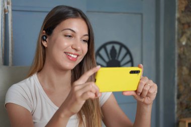 Kulaklıklı Brezilyalı kız oturma odasındaki kanepede oturmuş video paylaşım platformunda yayın izliyor. Cep telefonuyla evdeki kadın video görüşmeleri.