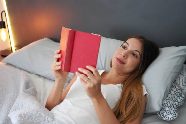 Evdeki boş günümde yatakta kitap okuyan mutlu genç bir kadın.