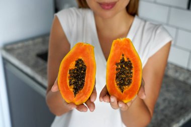 Kimliği belirsiz genç bir kadın mutfakta iki parçaya bölünmüş bir papaya gösteriyor.