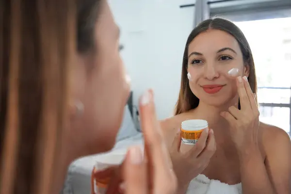 Skin care woman applying cream on her cheek. Face moisturizing antioxidant nourishing treatments. Enjoying relaxing time.