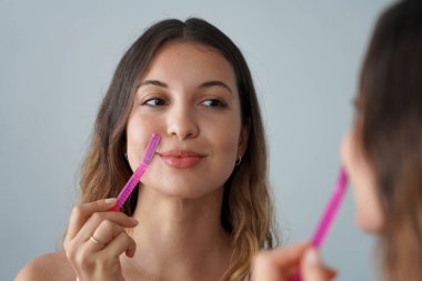 Dermplaning. Güzel bir kızın evde jiletle yüzünü tıraş edişinin yakın çekimi. Güzel kadın banyoda jilet kullanıyor..