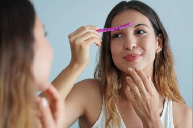 Dermplaning. Güzel genç bir kadın evdeki aynada jiletle kaşlarını tıraş ediyor. Yüz kılları alınıyor..