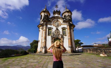 Tourism in Ouro Preto, Brazil. Back view of young tourist woman in Ouro Preto visiting Saint Francis of Assisi church in Minas Gerais state, Brazil. UNESCO world heritage. clipart