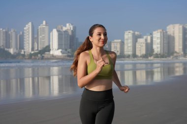 Fitness kızı sabahın erken saatlerinde plajda koşar. Arka planda ufuk çizgisi vardır.