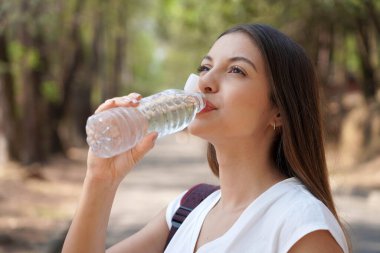 Plastik şişeye bağlı kapak. Geri dönüşümü teşvik etmek için yeni bir kapakla plastik şişeden su içen genç bir kadın, çöplere karşı verilen mücadelenin bir parçası olarak.