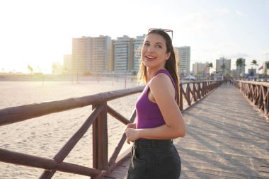 Güzel gülümseyen Brezilyalı kızın portresi Aracaju sahilinde gün batımında İskelede yürüyen kameraya doğru döner, Sergipe, Brezilya