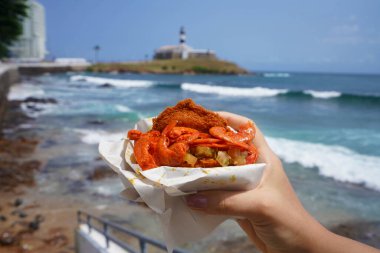 Kuzeydoğu Brezilya 'dan geleneksel yemek ve sokak yemekleri. Arka planda Farol da Barra Feneri ve All Saints Körfezi, Salvador de Bahia, Brezilya