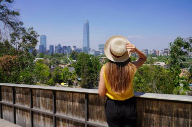 Santiago de Chile 'in ufuk çizgisinde Gran Torre Santiago ve And Dağları, Santiago, Şili, Güney Amerika' yla eğlenen genç bir gezginin arka görüntüsü.