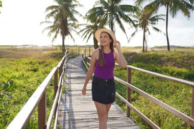 Summer holidays in Aracaju, Brazil. Brazilian girl with purple tank top walking on pier in Aracaju, Sergipe, Brazil. clipart