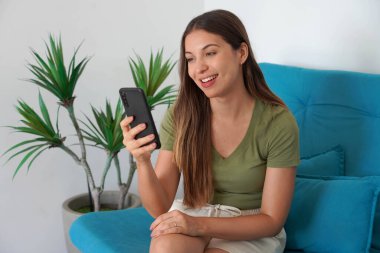 Brezilyalı kız evdeki kanepesinde sohbet etmek için akıllı telefon uygulaması kullanıyor.