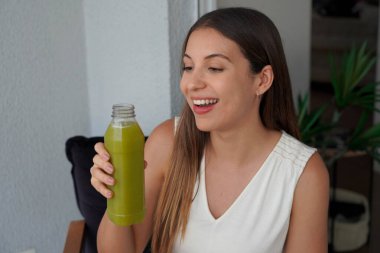 Elinde bir şişe yeşil smoothie detoks suyu tutan sağlıklı bir kadının portresi. Şişeye bakıyorum..