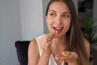 Güzel kız evde çerez olarak fındık yiyor. Yan tarafa bakıyor. Boşluğu kopyala.