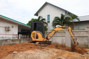 Bir kazıcı, bir evin beton sütunlarının temelini atmak için inşaat alanında toprak kazıyor.