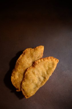 Kahverengi arka planda Cheburek. Et ve soğanlı kızarmış turta. Geleneksel Türk, Moğol, Doğu Tatar, Kafkas mutfağı. Yukarıdan bak. Boşluğu kopyala.