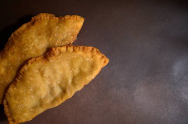 Kahverengi arka planda Cheburek. Et ve soğanlı kızarmış turta. Geleneksel Türk, Moğol, Doğu Tatar, Kafkas mutfağı. Yukarıdan bak. Boşluğu kopyala.