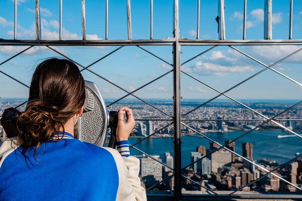 Rear view of girl looking at view of manhattan skyline with binoculars from the Empire State Building. High quality photo