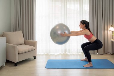 Asyalı kadın yatak odasında egzersiz yapıyor ve esniyor. Yoga, kardiyo ve karantina arasında evde spor yaparak zayıflamaya çalışıyor.