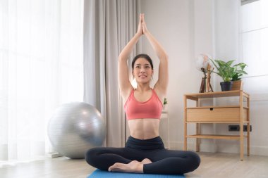 Asyalı kadın yatak odasında egzersiz yapıyor ve esniyor. Yoga, kardiyo ve karantina arasında evde spor yaparak zayıflamaya çalışıyor.