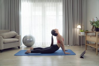 Asyalı kadın yatak odasında egzersiz yapıyor ve esniyor. Yoga, kardiyo ve karantina arasında evde spor yaparak zayıflamaya çalışıyor.