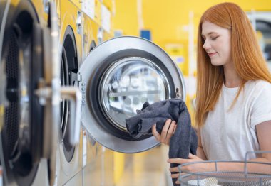 European woman washing her clothes by a washing machine in laundry shop clipart