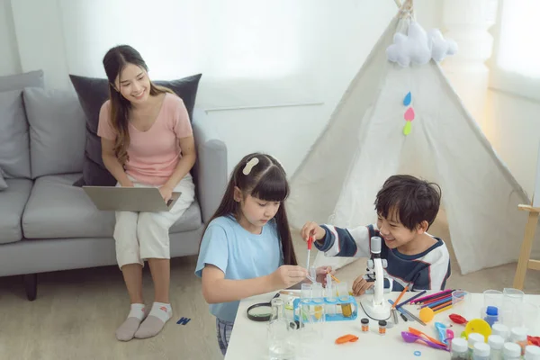 Asian mother play and learn together with her som and her daughter in living room, they play laboratory together