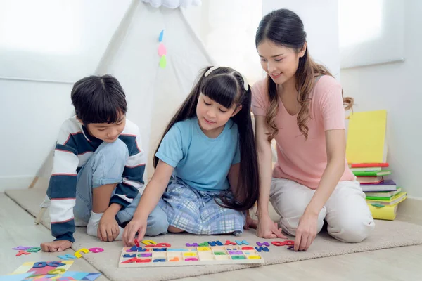 アジアの母親は遊び 彼女の息子と彼女の娘と一緒にリビングルームで学び 彼らは一緒にテキストブロックを再生します — ストック写真