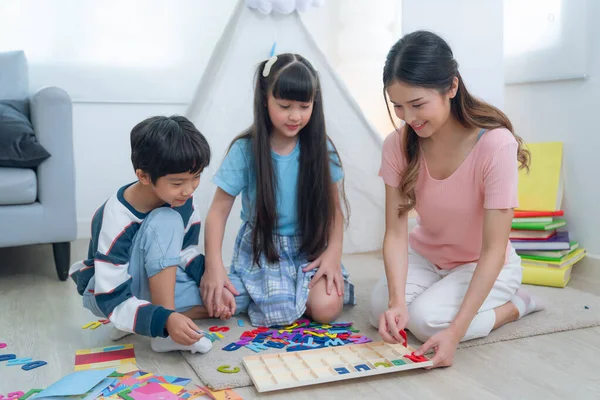 Asian mother play and learn together with her som and her daughter in living room, they play text block together