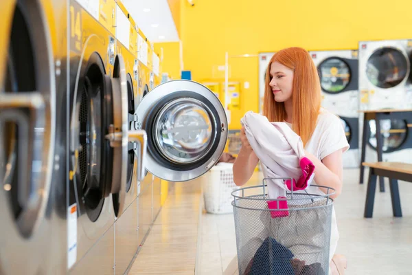 European woman washing her clothes by a washing machine in laundry shop