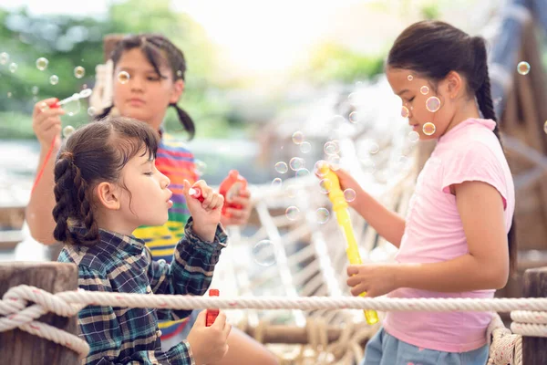 アジアの就学前の女の子のグループは 緑色の夏の自然背景と遊び場でおもちゃを吹くことによってシャボン玉を再生 — ストック写真
