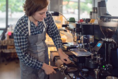 Women barista in an apron making coffee with coffee maker machine in a coffee shop