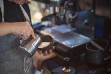 Close up Barista in an apron making coffee and make a milk topping with coffee maker machine in a coffee shop