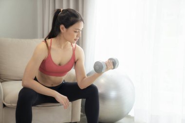 Asyalı kadın yatak odasında egzersiz yapıyor ve esniyor. Yoga, kardiyo ve karantina arasında evde spor yaparak zayıflamaya çalışıyor.