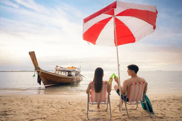 在泰国普吉岛附近的菲菲岛上 一对亚洲游客夫妇坐在一起 看着夕阳西下的落日聚集在沙滩上 背负着长尾船的背景 — 图库照片