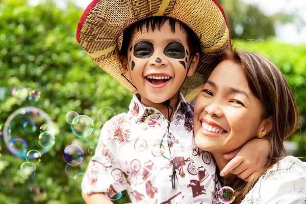 万圣节那天 亚洲男孩和他的母亲高兴地在花园里和户外打泡 脸上涂满了彩绘 — 图库照片
