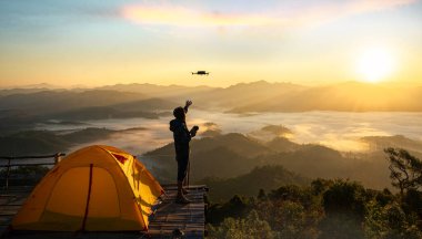 Bir adam, Tayland 'ın Chiang Mai yakınlarındaki Tak dağının zirvesinde güneşin doğuşuyla sisli arka plan arasında fotoğraf çekmek için insansız hava aracı kullanıyor.