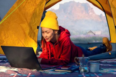 Çalışan bir kadın kahve içiyor ve bilgisayar not defteriyle çalışıyor yaz ve dağ saatleri arasında kamp kuruyor.
