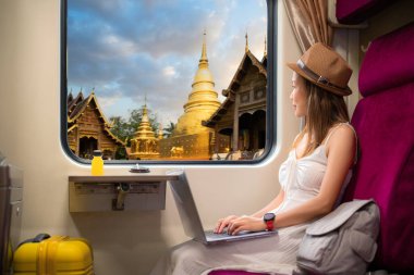 Asyalı gezgin kadın tren koltuğunda oturur ve Chiang Mai, Tayland 'daki Wat phra singh tapınağı manzaralı tren penceresinden dışarı kilitlenir.