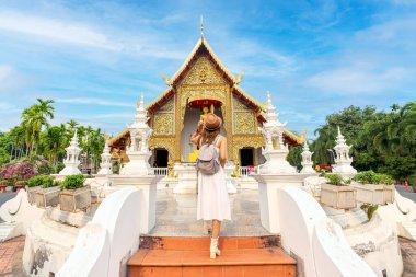 Beyaz seyahat elbisesiyle caddede yürüyen Asyalı gezgin Wat phra singh tapınağının önünde abd bagaj çantası, Chiang Mai, Tayland
