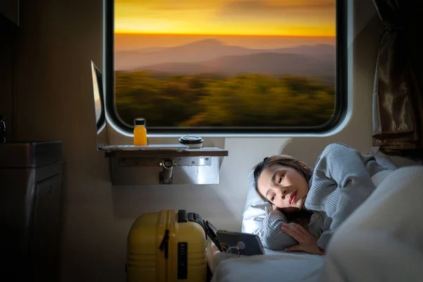 stock image Asian traveller woman sleep and washing TV by her smartphone on the train seat between her travel trip with sunset view in train windows