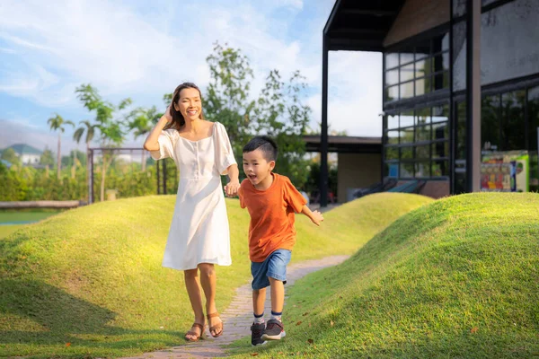 亚洲的母亲和她的小儿子跑到花园里用绿草聚集在一起 — 图库照片