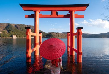 Kimonolu Asyalı bir çift kırmızı şemsiyeli ve kırmızı torii kapılı bir araya geldiler. Tokyo City, Japonya