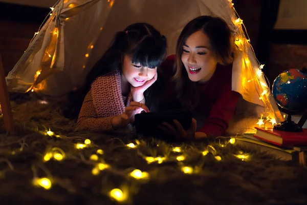亚洲的母亲和女儿们带着帐篷和灯光在卧室里放松一下 晚上回家的时候读些电子书 — 图库照片